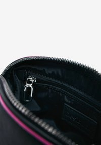 Black zippered bag interior with pink trim, featuring a small clipped attachment and a fabric label. Smooth texture and structured shape.