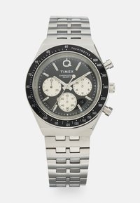 Silver stainless steel chronograph watch with a black and white dial, tachymeter bezel, and four sub-dials. Textured link bracelet.