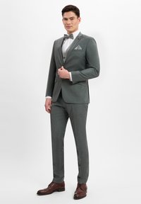 Gray tailored suit with a bow tie and pocket square. Features a modern fit and subtle texture. Brown leather shoes complete the ensemble.