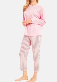 Roze katoenen langemouwtop gecombineerd met cropped gestreepte pyjamabroek met verticale lijnen in roze, blauw en wit. Bloten voeten.
