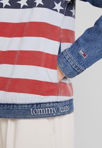 Chaqueta de mezclilla con rayas horizontales rojas y blancas y un patrón de estrellas azules encima. "Tommy Jeans" bordado en blanco en el dobladillo.