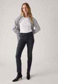 Camisa de botones a rayas sobre una camiseta blanca sin mangas, combinada con jeans negros de cintura alta y botas negras hasta el tobillo. Tejido suave y corte entallado.