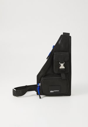 Črna torba za čez ramo z teksturirano obdelavo, ima sprednji žep z zadrgo, nastavljiv trak, kovinske detalje in modre akcentne podrobnosti.