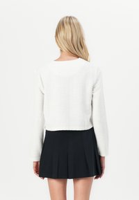 Weißer, taillierter Blazer mit langen Ärmeln, strukturierter Stoff, runder Halsausschnitt, kombiniert mit einem schwarzen Faltenrock, der ein einfaches Design zeigt.