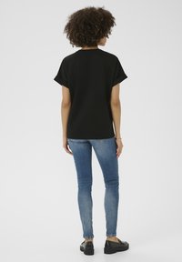 Juoda trumpa rankovėmis palaidinė su laisvu kirpimu, derinama su mėlynomis siaurėjančiomis kelnėmis ir juodais platforminiais batais. Minimalistinis ir kasdienis dizainas.