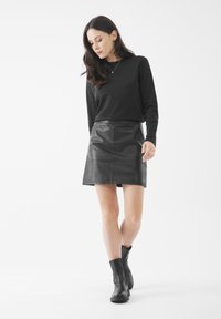 Mini falda de cuero negro con una textura suave y un diseño ajustado, combinada con una camiseta de manga larga negra y botines.