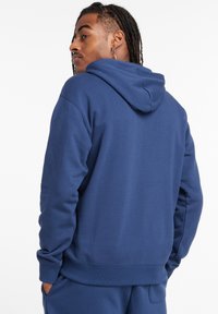 Hoodie blu navy con una vestibilità comoda, cappuccio regolabile con cordino e polsini a costine. Presenta un tessuto morbido e un design senza cuciture.