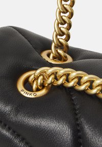 Zwarte leren handtas met een gequiltde textuur, goudkleurige hardware en een gedraaide kettinghengsel met ronde eyelet-details.