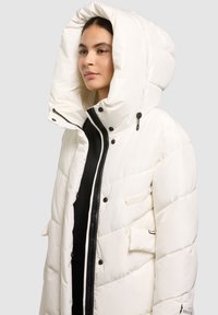 Geacă albă matlasată cu glugă largă, închideri cu capse și fermoar, având fermoar negru, buzunare exterioare și o textură matlasată.