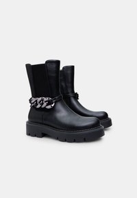Botines de cuero negro con suela gruesa, que cuentan con un acento decorativo de cadena y paneles elásticos laterales para facilitar el calzado.