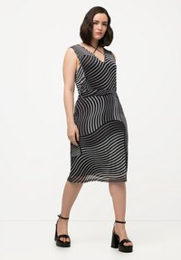 Vestido con rayas onduladas en blanco y negro, escote en V y cintura entallada. Combinado con sandalias de tacón grueso. Textura de tela suave.