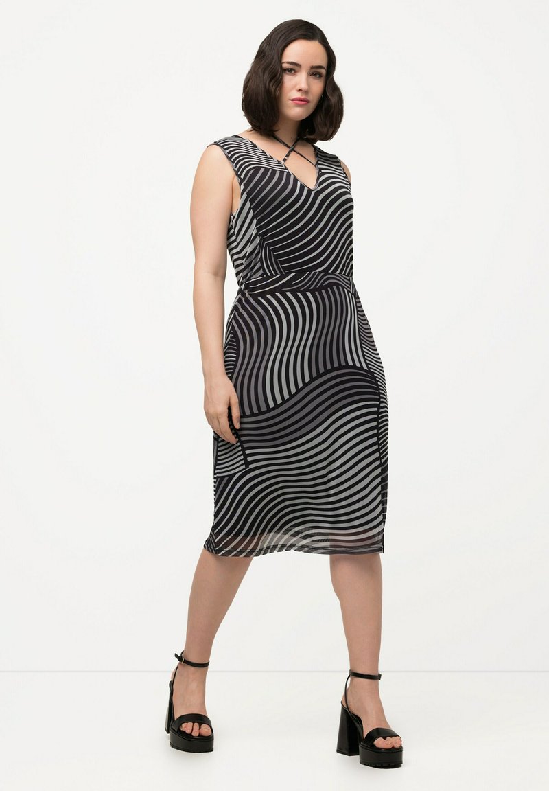 Vestido con rayas onduladas en blanco y negro, escote en V y cintura entallada. Combinado con sandalias de tacón grueso. Textura de tela suave.