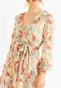 Floral wrap dress in lightweight fabric, featuring a v-neck, balloon sleeves, a belted waist, and a multicolored floral pattern on a light background.
