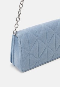 Borsa in denim blu trapuntato con motivo triangolare, dotata di una tracolla in metallo argentato e un design strutturato. Texture liscia e forma rettangolare.