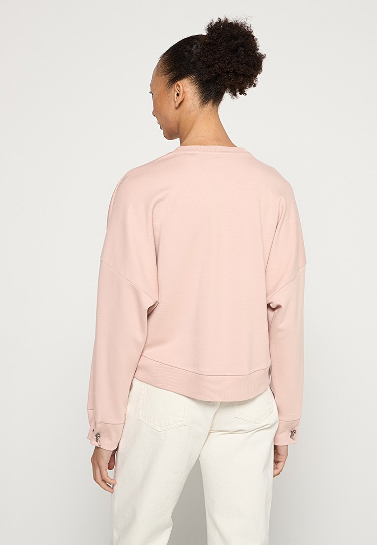 Helles rosa Sweatshirt mit einem cropped Design, lockerer Passform, abgesenkten Schultern und geripptem Saum. Schlichtes Rundhals, weicher Stoff und geknöpfte Bündchen.