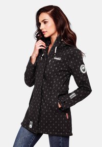 Black waterproof jacket with grey handprint pattern, adjustable hood, zippered pockets, and logo details. Features a fitted silhouette.