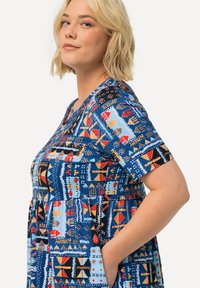 Värikäs sininen lyhythihainen mekko, jossa on monivärisiä geometrisiä kuvioita, taskut ja rento istuvuus pyöreällä kaula-aukolla.