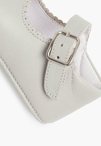 Zapato de cuero gris claro con puntera redonda, bordes festoneados y hebilla plateada. Textura suave y diseño simple.