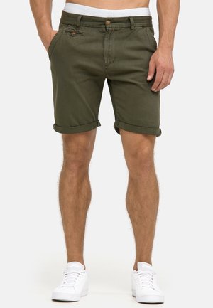 Khakifarbene Baumwollshorts mit umgeschlagenen Säumen, Vorderentaschen und einem Knopfverschluss. Tragen mit weißen Sneakers vor einem schlichten Hintergrund.