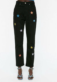Vaqueros de mezclilla negra con aplicaciones de estrellas multicolores en azul, naranja, amarillo y púrpura. Corte recto con diseño de cinco bolsillos.