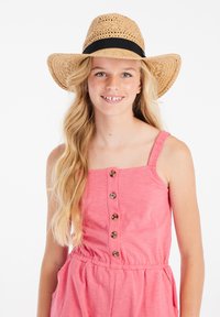 Sombrero de paja con una banda negra en una niña que lleva un mono sin mangas rosa con botones en la parte delantera y una cintura elástica.