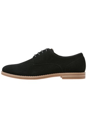 Black suede men's lace-up dress shoe with light brown sole and low heel, side profile on white background.