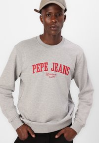 Szürke kapucnis pulóver piros logós szöveggel: "PEPE JEANS London 1973", bordás mandzsettákkal és derékpánttal.