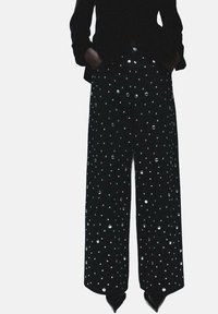Pantalones negros de pierna ancha con un acabado texturizado, adornados con lunares plateados, con cintura alta y bolsillos.