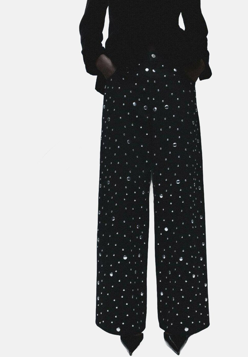 Pantalones negros de pierna ancha con un acabado texturizado, adornados con lunares plateados, con cintura alta y bolsillos.