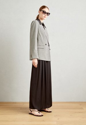 Šedá houndstooth dvouřadá sako, černá košile pod ním, splývavá černá maxi sukně a ploché černé sandály, doplněné o velké sluneční brýle.