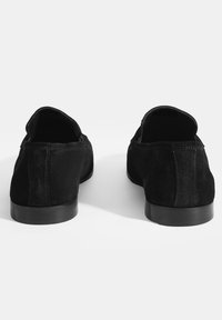 Schwarze Wildleder-Loafer mit niedrigem Absatz, die eine glatte Textur, eine abgerundete Form und minimale Nähdetails auf der Rückseite aufweisen.