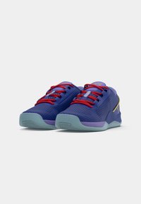 Scarpe da ginnastica viola con tomaia in rete, lacci rossi e suola azzurra chiara. Presentano motivi testurizzati e accenti a contrasto.