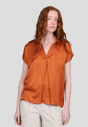 Blouse satin couleur rouille avec un décolleté en V, des manches courtes retroussées et une coupe ample. Texture lisse avec un détail plissé à l'avant.