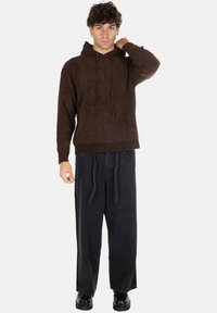Felpa con cappuccio marrone lavorata a maglia, con tasca frontale, cordini regolabili e polsini a coste, abbinata a pantaloni in denim neri larghi e scarpe nere.