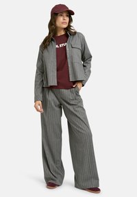 Gray striped jacket and matching wide-leg pants over a burgundy t-shirt, complemented by a burgundy cap. Soft fabric texture, casual fit.