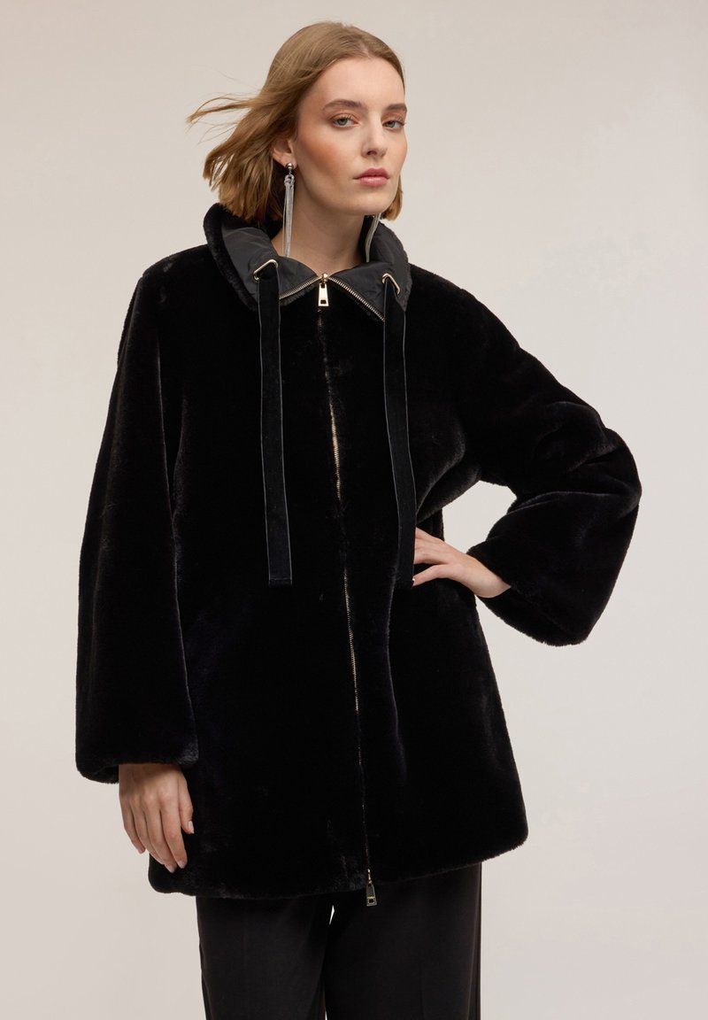 Czarny płaszcz ze sztucznego futra z odpinanym szarym kapturem, zamkiem błyskawicznym z przodu i sznurkami do zaciągania. Luźny krój z szerokimi rękawami i gładką fakturą.