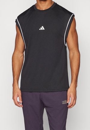 Mężczyzna noszący czarną sportową koszulkę bez rękawów Adidas z białym obszyciem oraz fioletowe spodnie do koszykówki Adidas.