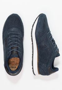 Para granatowych zamszowych tenisówek z fakturowaną cholewką, czarno-białą podeszwą z bieżnikiem i korkowymi wkładkami, pokazanych z widoku z góry i z boku.