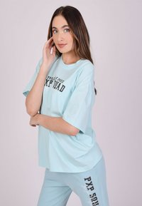 Camiseta oversized de color azul claro en tela suave con cuello redondo y un estampado gráfico. Combinada con pantalones ajustados a juego con texto lateral.