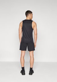 Schwarzes ärmelloses Tanktop und passende Shorts an einer Person, mit glattem Material und sportlichem Schnitt, von hinten gezeigt.