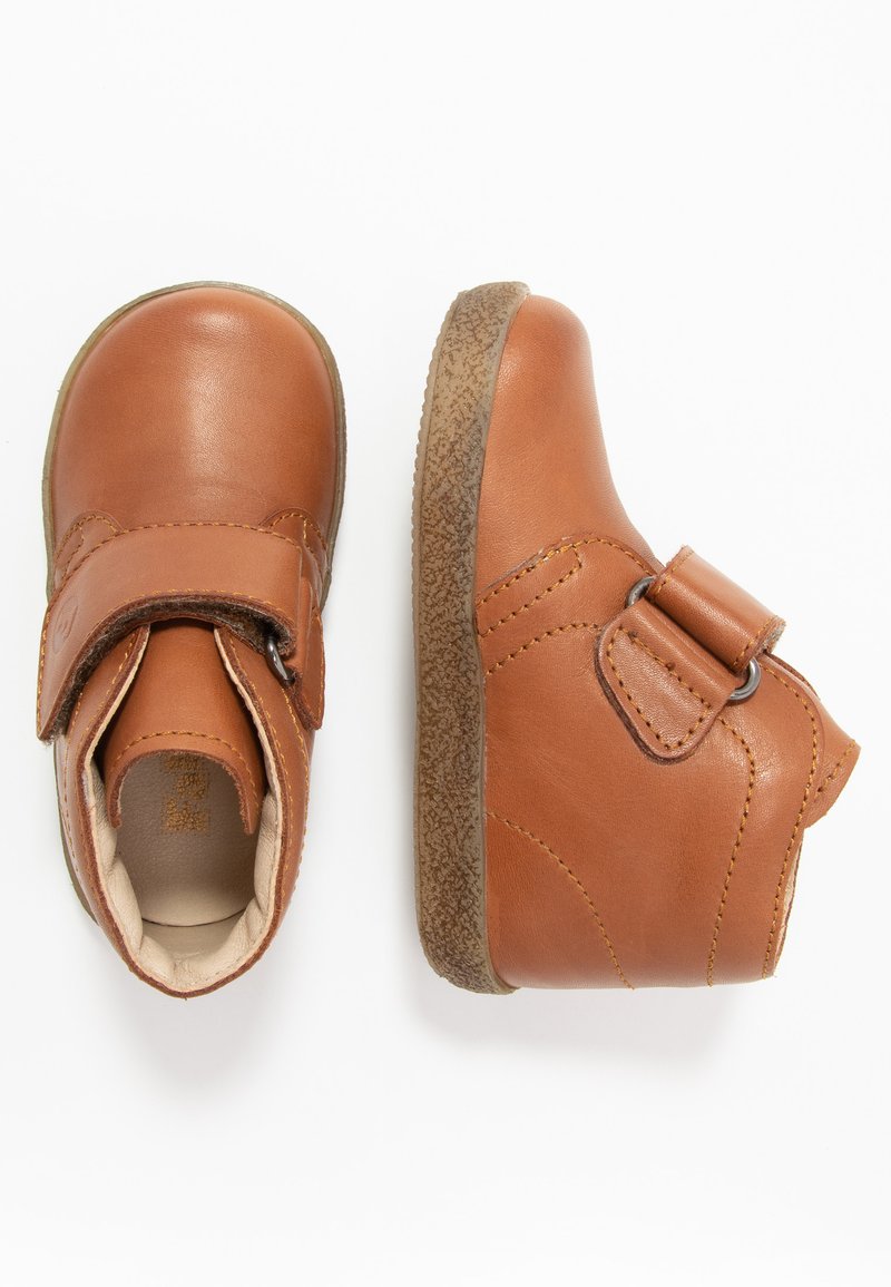 Bottines en cuir marron avec une sangle en Velcro, bout rond et semelle en caoutchouc texturée. Accents de couture sur la tige.