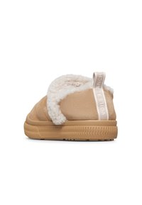 Scarpa slip-on beige con morbido rivestimento bianco, suola in gomma e linguetta in tessuto sul tallone con testo su sfondo bianco.
