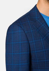 Granatowa marynarka w kratę z niebieskim i czarnym wzorem, z wyraźnymi ramionami, miękkiego materiału i szczegółowymi szwami.