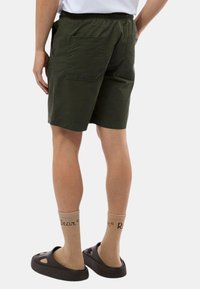 Pantaloni corti color khaki con cintura elastica, due tasche posteriori e vestibilità comoda. Indossati con zoccoli marroni e calze a coste beige.