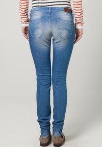 Smala blå jeans i denim med en urtvättad finish, två bakfickor och en brun läderflik vid midjan.