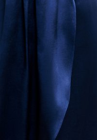 Detailní záběr na tmavě modrou sametovou látku s jemnými sklady a subtílním leskem, který zvýrazňuje texturu.