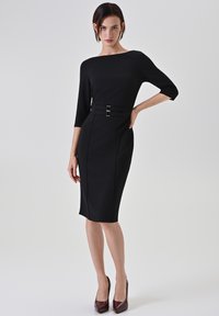 Robe noire ajustée avec manches trois-quarts, encolure bateau et une double boucle à la taille ; texture lisse, longueur au genou.