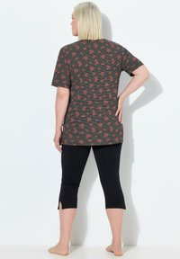 Camiseta de rayas en blanco y negro con un patrón floral rojo, combinada con pantalones capri negros que tienen aberturas laterales para ventilación.