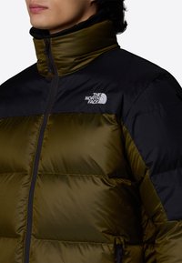 Kurtka puchowa w zielono-czarnym kolorze z wysokim kołnierzem, ribbową teksturą i logo na lewej piersi. Zapięcie na zamek błyskawiczny.