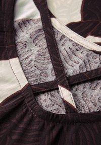 Tissu avec des motifs de feuilles marron complexes sur un fond clair, présentant un col rond et des détails de couture contrastés.